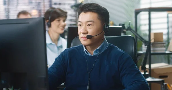 Närbild porträtt av asiatiska glada stilig manliga call center operatör sitter vid bordet på företagets kontor i headset tittar på kameran och ler. Glad man anställd på arbetsplatsen, arbetskoncept — Stockfoto