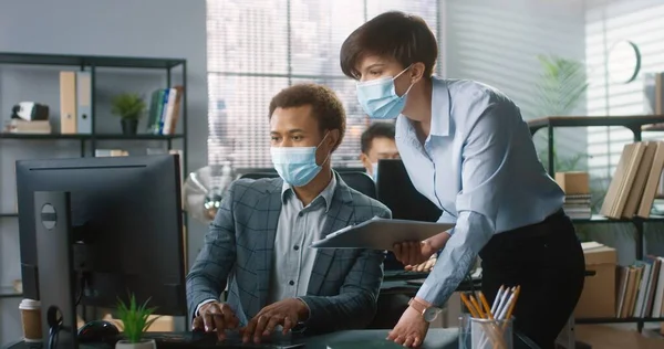 의료 마스크를 쓰고 있는 백인 여성 과 대화를 나누고 있는 아프리카 계 미국인 청년의 모습 문서를 보고 사무실에서 컴퓨터를 사용하는 사업 프로젝트에 대해 토론하고 있는 장면 — 스톡 사진