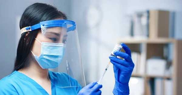 アジアの若い美しい女性の医療専門家は、医療用マスクを身に着けており、病院のアンプルからコロナウイルスワクチンで注射器を充填顔シールド。鳥の予防接種の概念を閉じて — ストック写真