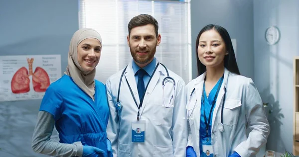 Portrait of happy joyful young professional physicians standing in hospital looking at camera and smiling. Team of healthcare workers doctors in clinic in good mood. Medical center, job concept — Stock Photo, Image