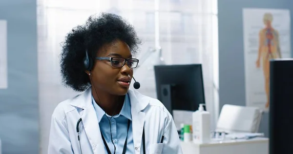 Nahaufnahme Porträt einer fröhlichen hübschen jungen afroamerikanischen Gesundheitsexpertin, die im Headset auf einem medizinischen Online-Webinar am Computer spricht, Videoberatung im Internet, medizinisches Konzept — Stockfoto