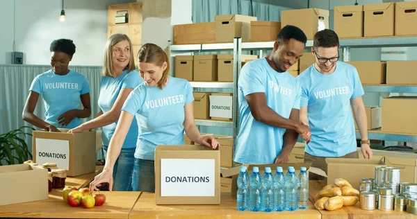 Raza mixta feliz positivo masculino y femenino diferentes voluntarios que trabajan en el centro de organización benéfica preparando y empacando caja de ayuda social, caja de donaciones, voluntariado y concepto de donación —  Fotos de Stock