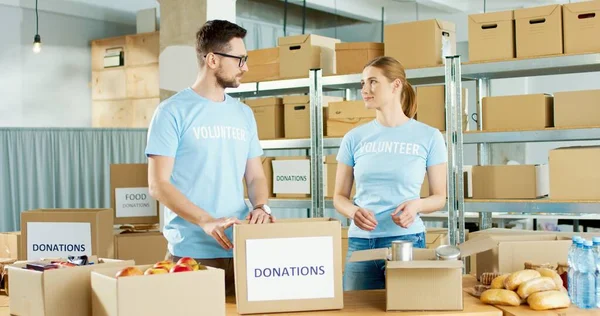 Caucasian young male and female volunteers putting food products in box sorting donations parcel working in charitable stock organization. Charity workers, social organization, volunteering — Stock Photo, Image