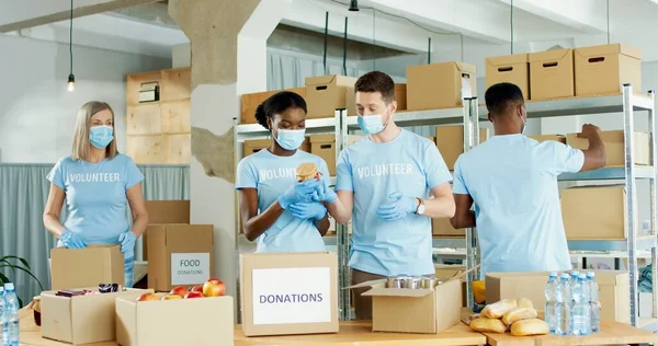 Diversas pessoas mestiças homens e mulheres que trabalham em armazéns em organizações de caridade coletando e classificando doações preparando caixas de ajuda social com alimentos. Voluntários, serviço social, doação — Fotografia de Stock