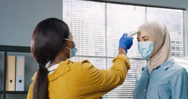 Tıbbi maske takmış Afrikalı Amerikalı bir kadın Coronavirus salgını sırasında kızılötesi termometre kullanarak işçileri kontrol ediyor. Kapatın, karantina konsepti