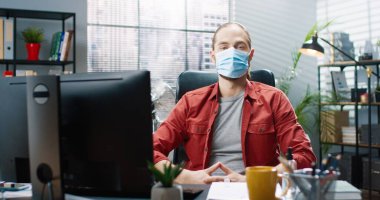 Kabine masasında oturan beyaz, mutlu ve yakışıklı bir erkek çalışanın portresi tıbbi maskeyi yüzünden çıkarıyor, kameraya bakıyor ve gülümsüyor. Ofis işi tarzı. Coronavirus karantina işi