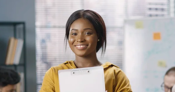 Närbild porträtt av unga afroamerikanska glada positiva kvinnliga anställd står i skåp på jobbet, tittar på kameran och ler. Glädjande kvinnlig arbetare med leende i ansiktet, ockupationskoncept — Stockfoto