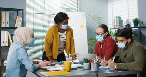 Jóvenes diferentes empleados multiétnicos en máscaras médicas se reunieron trabajando en el gabinete tocando en el ordenador portátil y la navegación en el teléfono inteligente discutir el problema de negocios Los trabajadores ocupados en la oficina Concepto de trabajo —  Fotos de Stock