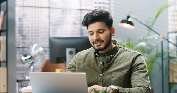 Närbild porträtt av glada hinduiska unga stilig kille arbetare videochattar talar på nätet samtal på laptop medan du sitter på arbetsplatsen på kontoret och ler hand. Framgångsrik affärsman — Stockfoto