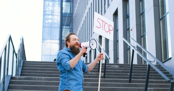 Μια διαμαρτυρία ενός Καυκάσου με γένια να μιλάει και να ουρλιάζει σε μεγάφωνο. Αντρας προτεστάντης κρατώντας τραπέζι Stop ενώ εφιστά την προσοχή στο πολιτικό ή περιβαλλοντικό ζήτημα. Μοναχική διαμαρτυρία. — Φωτογραφία Αρχείου