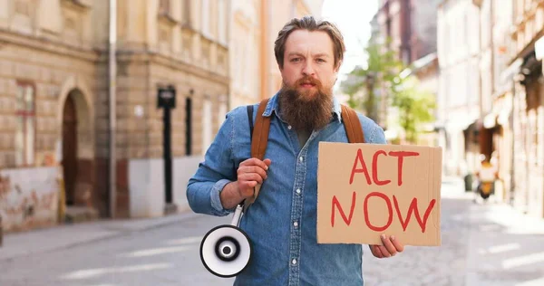 Portrait d'un militant masculin caucasien portant la barbe Loi maintenant et mégaphone lors d'une manifestation politique ou environnementale solitaire en ville. Une seule manifestation dehors. Homme protestant seul. — Photo