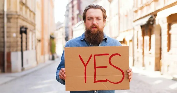 Πορτρέτο του Καυκάσου νεαρού άνδρα που στέκεται στο δρόμο στην πόλη και δείχνει αφίσα με "Ναι λέξη". Άντρας ακτιβιστής διαδηλώνει συμβούλιο με δήλωση συμφωνίας. — Φωτογραφία Αρχείου