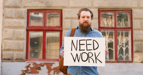 Portrét nezaměstnaného bělocha, jak stojí na ulici ve městě a ukazuje plakát se slovy Need Work. Mužská bezpracná demonstrační deska s oznámením. Osoba bez zaměstnání po uzamčení. — Stock fotografie