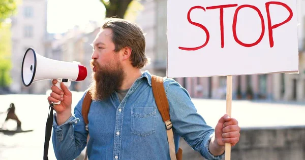 Közelkép kaukázusi férfi aktivistáról, szakállas sikoltozó hangosbeszélővel. Ember kezében poszter Állj meg a politikai vagy környezeti magányos demonstráció. Egyetlen tiltakozás a város főterén. — Stock Fotó