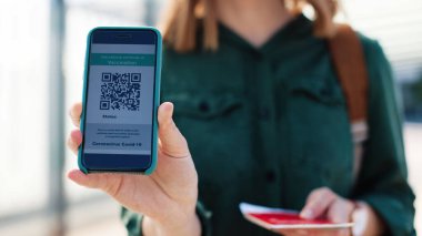 Covid-19 aşısını kanıtlayan sağlık pasaportlu, modern akıllı telefon taşıyan neşeli beyaz kadın yolcuları yakından takip edin. COVID aşı pasaportu. Güvenli seyahat tedbirleri