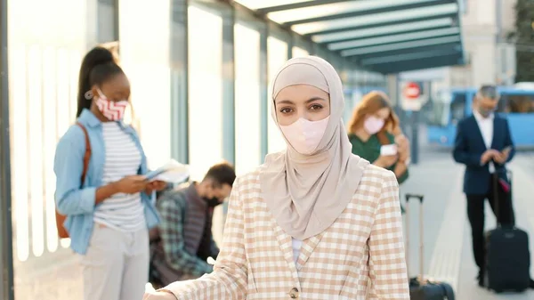 아름다운 이슬람 얼굴에 마스크를 정류장에서 밖에서 기다리고 카메라를 배경에 여행자 — 스톡 사진