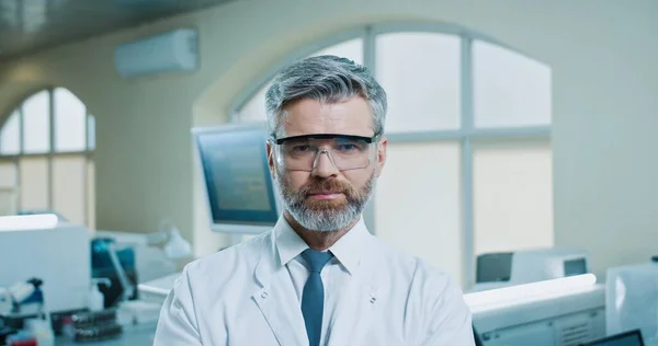 Nahaufnahme Porträt eines bärtigen kaukasischen Arztes mittleren Alters, der im klinischen Labor steht, in die Kamera schaut und lächelt. Schöner glücklicher Mann Laborspezialist am Arbeitsplatz im Krankenhaus. Sanitätskonzept — Stockfoto