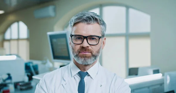 近照照片，照片上是快乐的白种人，蓄着胡子的资深男性专业医生，站在临床实验室里，看着镜头，微笑着。在医院实验室工作的漂亮快乐的员工 — 图库照片