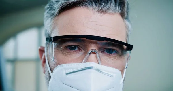 Freudig gut aussehender kaukasischer Arzt mittleren Alters, der im klinischen Labor eine Maske auf dem Gesicht trägt, in die Kamera schaut und während der Pandemie lächelt. Krankenhaus, Nahaufnahme, Coronavirus — Stockfoto