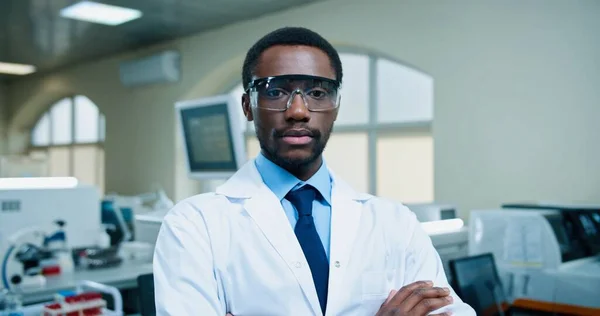 Porträt eines fröhlichen afroamerikanischen jungen, gut aussehenden Arztes mit Brille, der in die Kamera blickt und bei der Arbeit im Krankenhauslabor lächelt. Mediziner, Laborfachmann, Medizinkonzept — Stockfoto