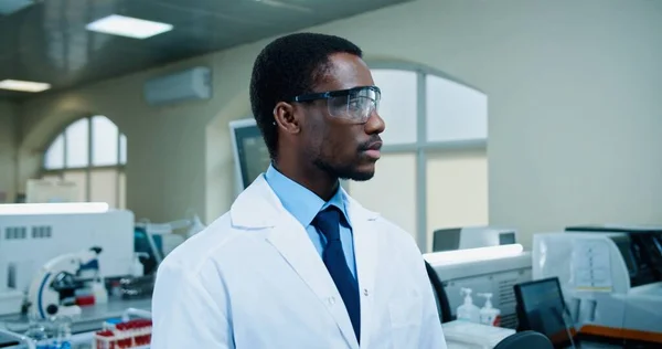 Porträt eines gut aussehenden afroamerikanischen jungen positiven männlichen Berufsmediziners mit Brille, der lächelnd in die Kamera blickt, als er am Arbeitsplatz im klinischen Labor steht. Laborspezialist im Krankenhaus — Stockfoto