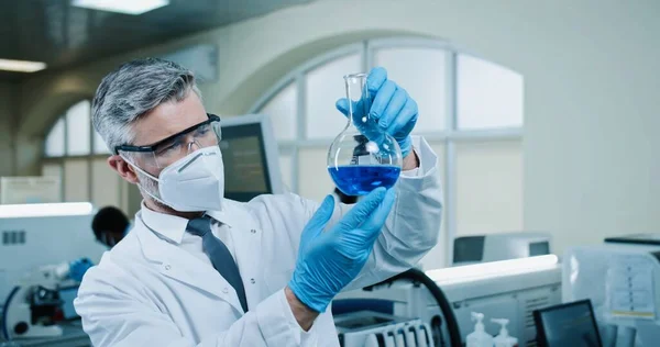 Close Middle Aged Caucasian Man Pharmacist Goggles Gloves Holding Glassware — Zdjęcie stockowe