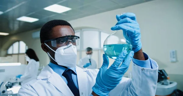 코트를 플라스크를 바라보며 실험중인 액체를 플라스크를 아프리카 미국인젊은 과학자의 사진을 — 스톡 사진