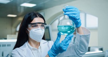 Caucasian beautiful woman chemistry researcher in sterile laboratory using glassware to test microbiology liquid. Close up of young female scientist working on virus cure in test tube working in lab