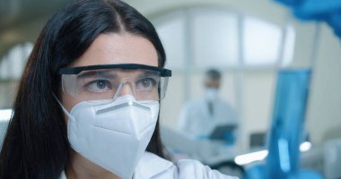 Close up of Caucasian beautiful woman chemistry researcher in laboratory working testing microbiology blue liquid Young female medical scientist working on coronavirus cure looking at test tube in lab