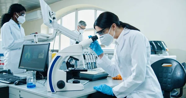 기술을 사용하여 실험실에 앉아마스크와 장갑을 현미경으로 실험하는 여성의 분석하는 실험실 — 스톡 사진
