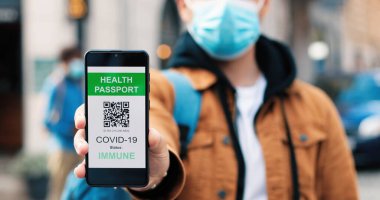 Kısa saçlı ciddi bir adamın portre görüntüsünü kapat. Sakince kameraya bakıyor ve Coronavirus salgını sırasında boş sokakta dururken akıllı telefonunda aşı pasaportunu gösteriyor.