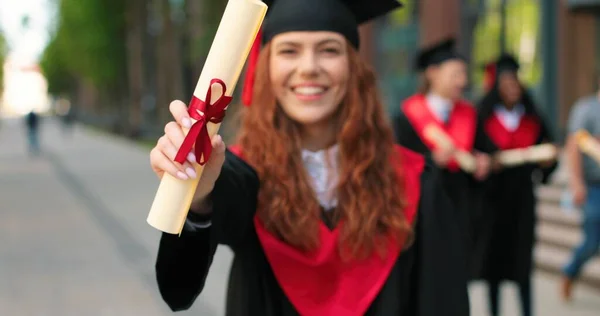 Young graduated girl holding her graduation degree convocation ceremony. Attractive student graduate posing towards the camera during the ceremony — Stock Fotó
