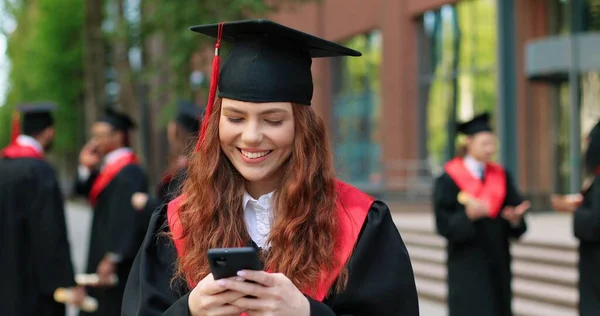 E-learning, educação e conceito de pessoas. Feliz sorridente caucasiano estudante de pós-graduação do sexo feminino em pé na rua com smartphone e digitando mensagem com prazer sorriso — Fotografia de Stock