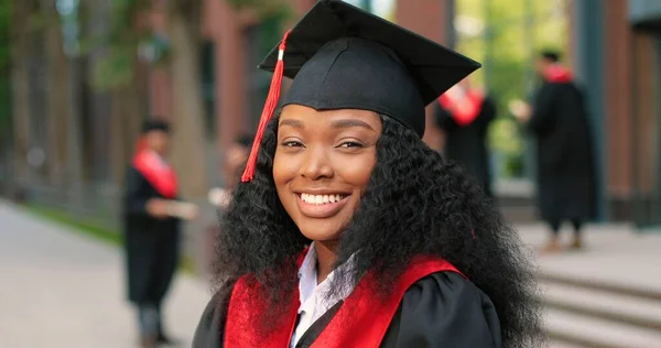 Young graduated curly girl holding her graduation degree convocation ceremony. Attractive multiracial student graduate posing towards the camera during the ceremony
