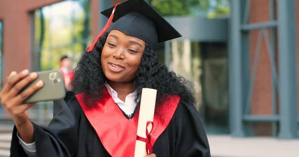 为从大学毕业的女毕业生树立形象，微笑着祝贺她大学毕业。女人通过视频通话与她的智能手机聊天 — 图库照片