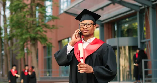 Sou formado. Estudante multirracial feliz chamando alguém com seu smartphone e se alegrando enquanto celebra sua formatura. Conceito de educação — Fotografia de Stock