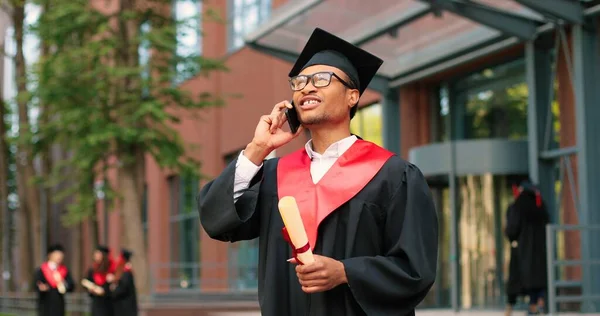 我毕业了。快乐的多种族学生用他的智能手机打电话给某人，在庆祝他的毕业典礼上欢欣鼓舞。教育概念 — 图库照片