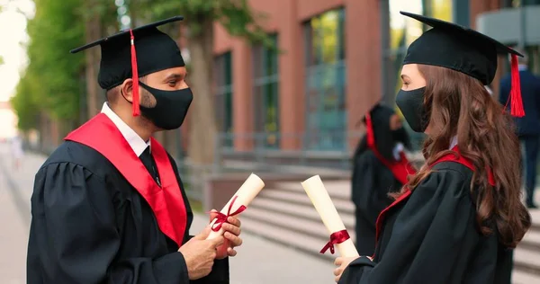 Waist up portrait view of the two students wearing protective masks greeting with elbows with each other and discussing their graduation during the covid 19 pandemic — ストック写真