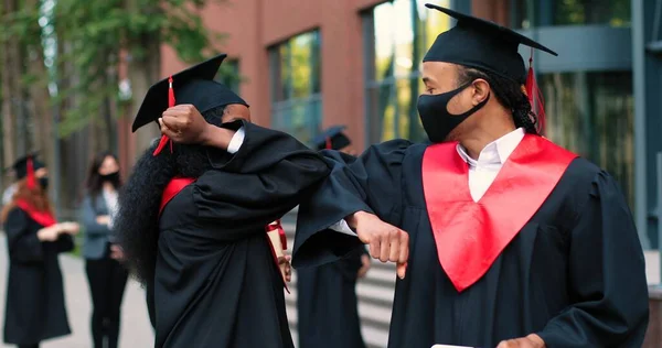 Neue Normalität. Porträtansicht der beiden Studenten mit Schutzmasken, die mit Ellbogen grüßen und über ihren Abschluss während der covid 19 Pandemie diskutieren — Stockfoto