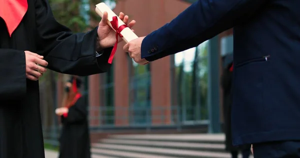 Cropped view of the two graduated students shaking hands to each other while standing near the university after the graduation. People holding their diplomas — ストック写真