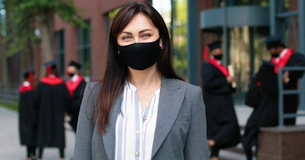 Porträtt utsikt över den lugna förtjusande mamma bär skyddande mask tittar på kameran och ler medan väntar sitt barn efter examen. Utbildningsidé — Stockfoto