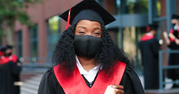 Visão de retrato da estudante multirracial usando chapéu preto e posando com certificado para a câmera porque ela se formou na universidade. Conceito de educação — Fotografia de Stock