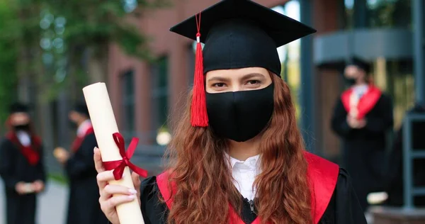Portrait view of the caucasian female student wearing black hat and posing with certificate to the camera because she graduated from university. Education concept