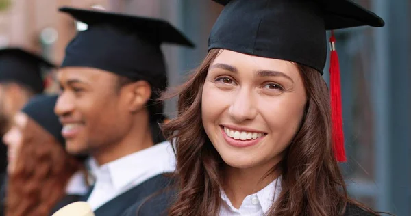 Glückliche Zeiten. Porträtansicht des brünetten, glücklichen Mädchens, das mit breitem Lächeln in die Kamera blickt, während sie mit ihren Klassenkameraden steht und der Abschlussrede ihres Lehrers lauscht. Bildungskonzept — Stockfoto