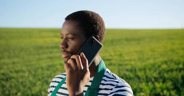 A multiracionális profi gazdatulajdonos portréja, aki egységes csevegést visel az okostelefonon, miközben ökológiai szántóföldi növénytermesztésen dolgozik. Mezőgazdasági és kertészeti koncepció — Stock Fotó