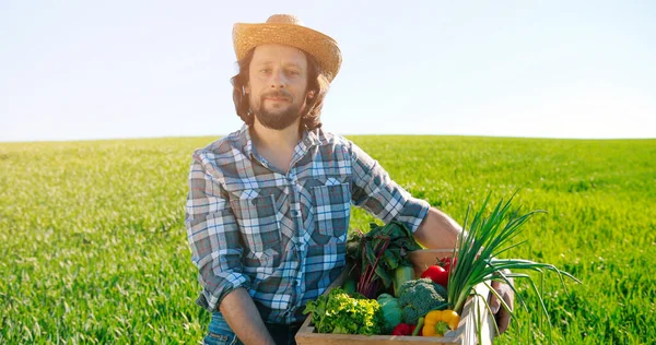 Caucasian tired farmer wearing hat walking out of rural field with fresh collected green vegetables. Harvesting foods. Domestic agribusiness. Organic food concept — Stock Photo, Image