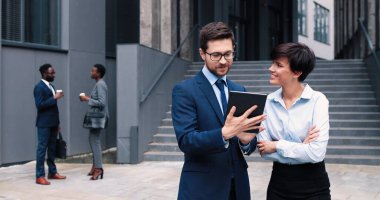 Kendine güvenen bir iş. Genç ciddi iş adamının belden yukarı portresi, ekrana dikkatle bakarken sevimli bayan meslektaşının yanında tabletle duruyor. İş konsepti