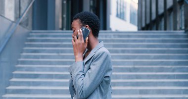 İş merkezinin yakınında yürüyen, resmi kıyafetler giyen çekici ve zarif bir kadının belden yukarı portre görüntüsü. Cep telefonunu elinde tutuyor ve zevkle sohbet ediyor.