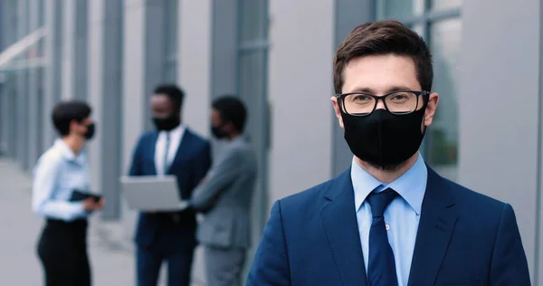 Midjan upp porträttvy över bra bärbar ung man bär glasögon och skyddsmask står utanför nära kontoret centrum. Han tittar på kameran och ler. — Stockfoto