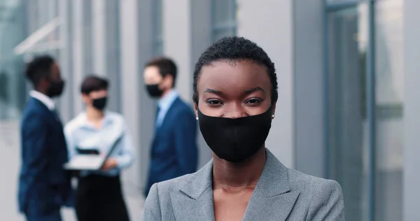 Başarılı olmak. Mutlu, çok kültürlü, koruyucu maske takan genç iş kadınının portresi, ofisin yanında dururken kameraya neşeyle bakıyor. — Stok fotoğraf